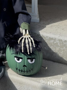 A cute Frankenstein Halloween decor placed on the front porch stairs with a skeleton hand on it's head.