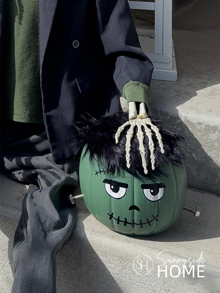 A cute Frankenstein Halloween decor placed on the front porch stairs with a skeleton hand on it's head.