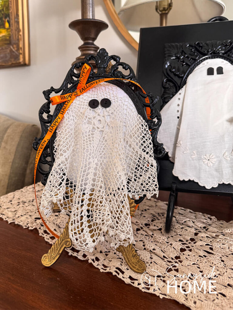 Styled DIY Halloween ghosts made with vintage doilies in thrifted frames, embellished with ribbon, buttons and felt.