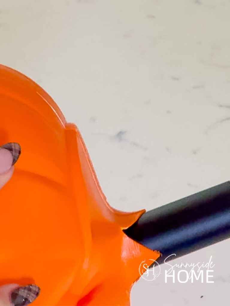 The stake of a solar light is pushed through the cut X in the bottom of an orange plastic pumpkin trick or treat bucket.