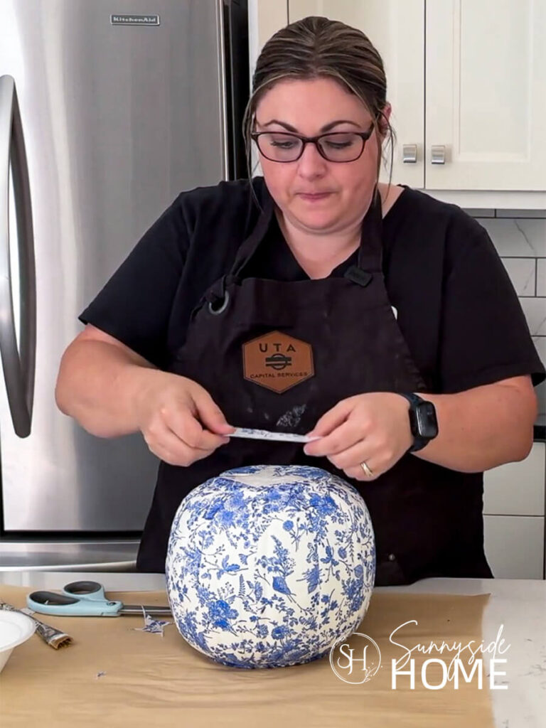 Woman places napkin on the top of the decoupaged pumpkin.