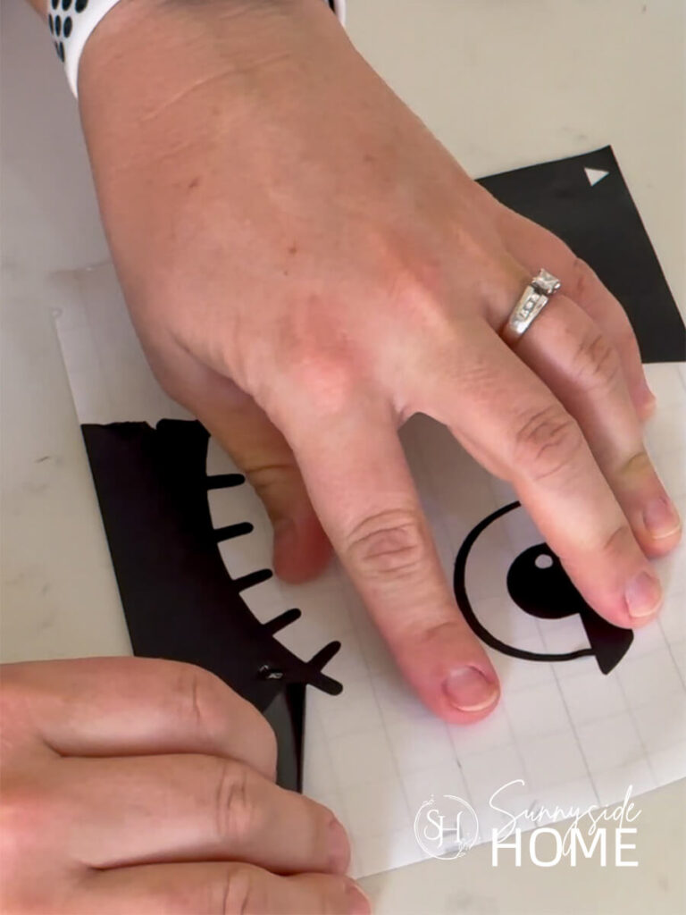 Woman's hands as she weeds the excess vinyl from a digital cut out of Frankenstein's face.