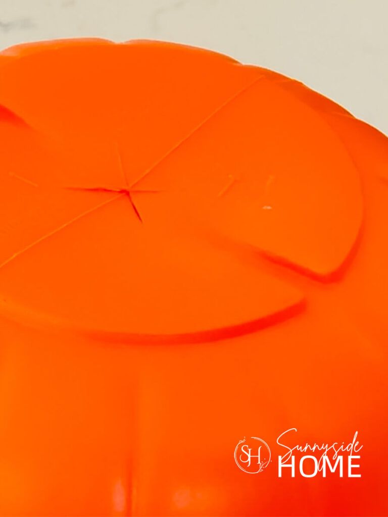 And X is cut into the bottom of an orange plastic trick or treat bucket.