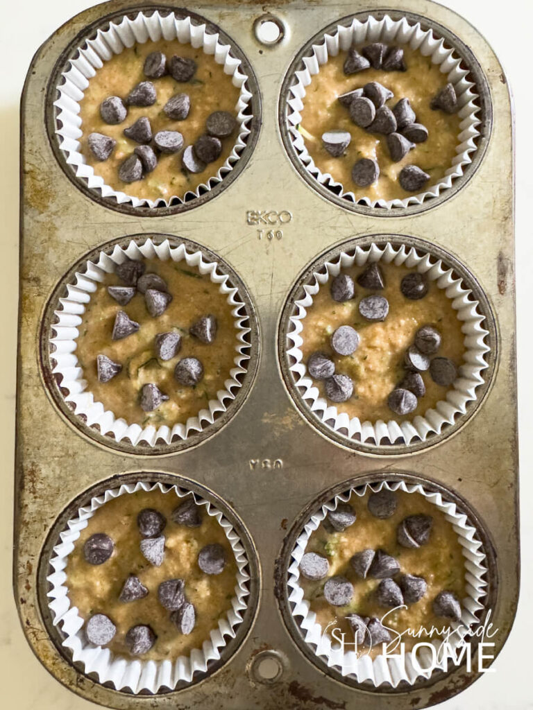 A muffin tin lined with paper liners and filled with protein zucchini muffin batter and sprinkled with sugar-free chocolate chips.
