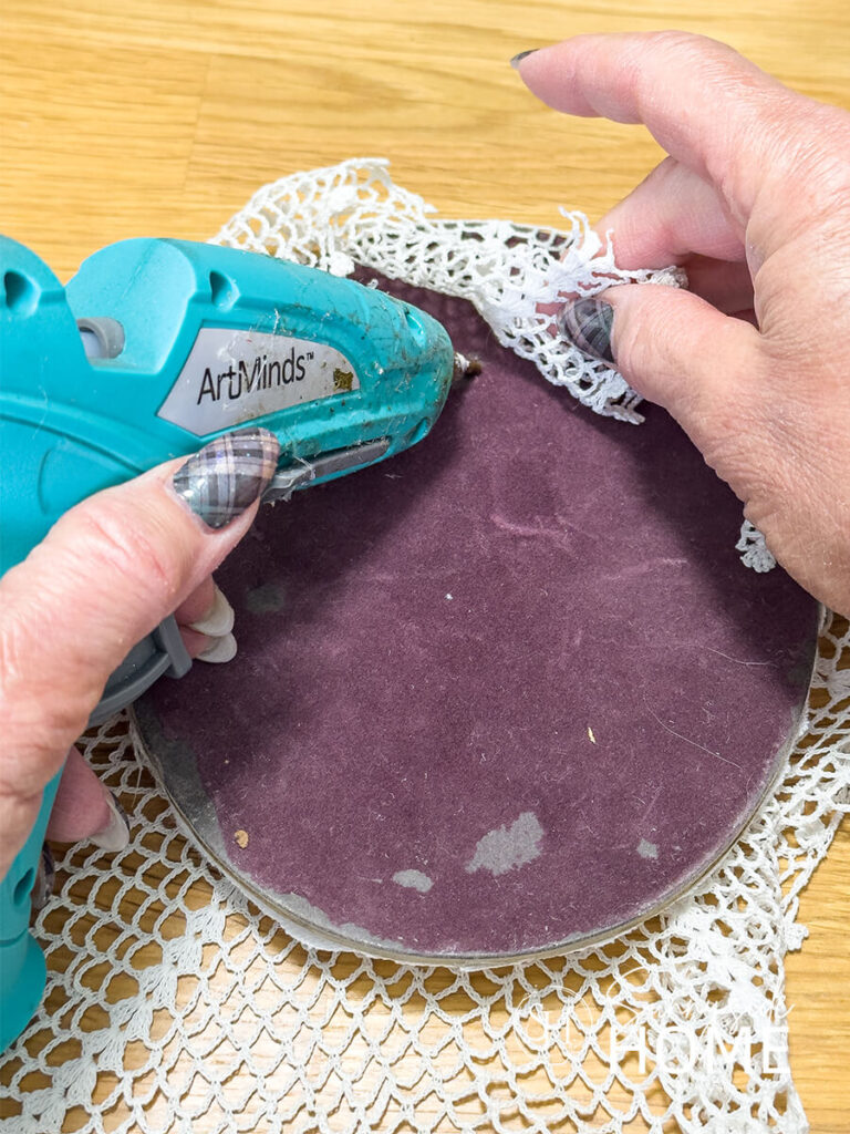 A woman adheres the doily to the back of the frame backing.