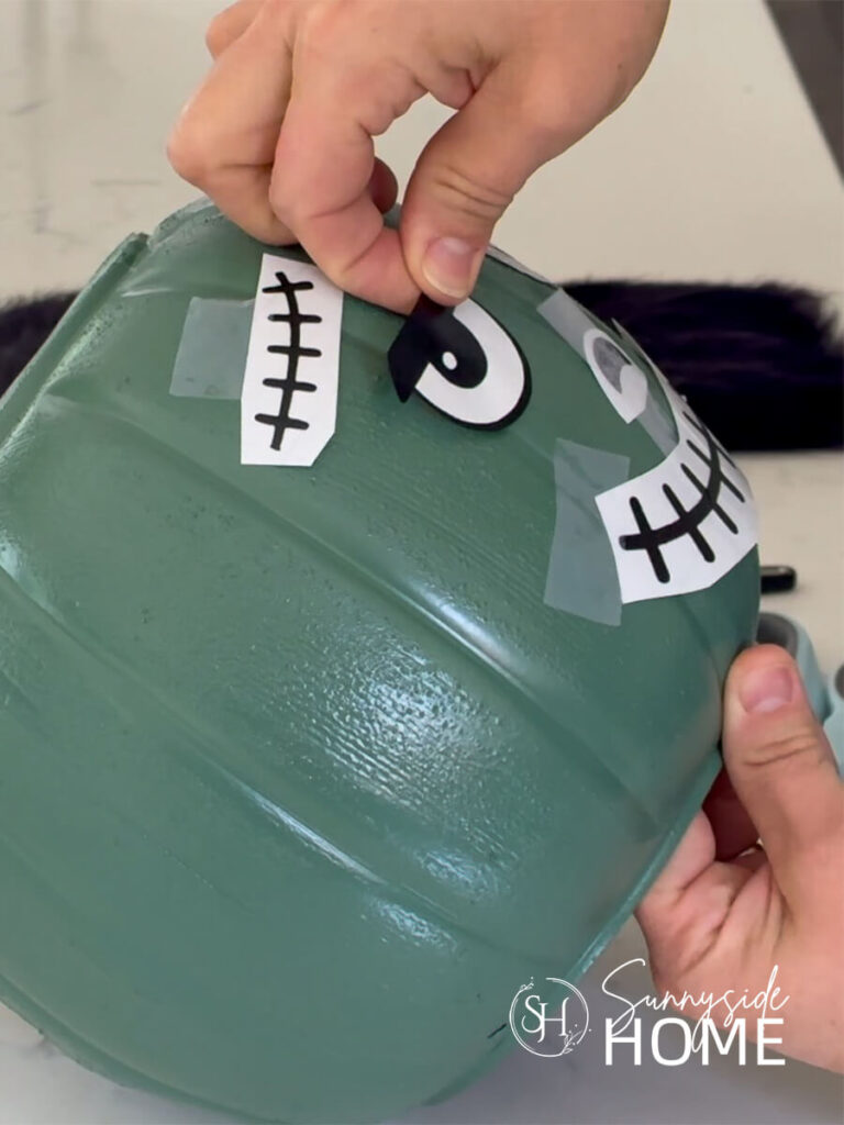 A woman places the vinyl face pieces onto a green painted halloween pumpkin bucket.