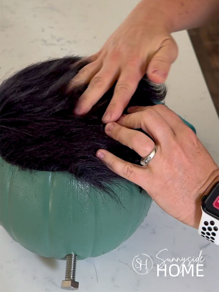 A woman glues black faux fur hair to Frankenstein.