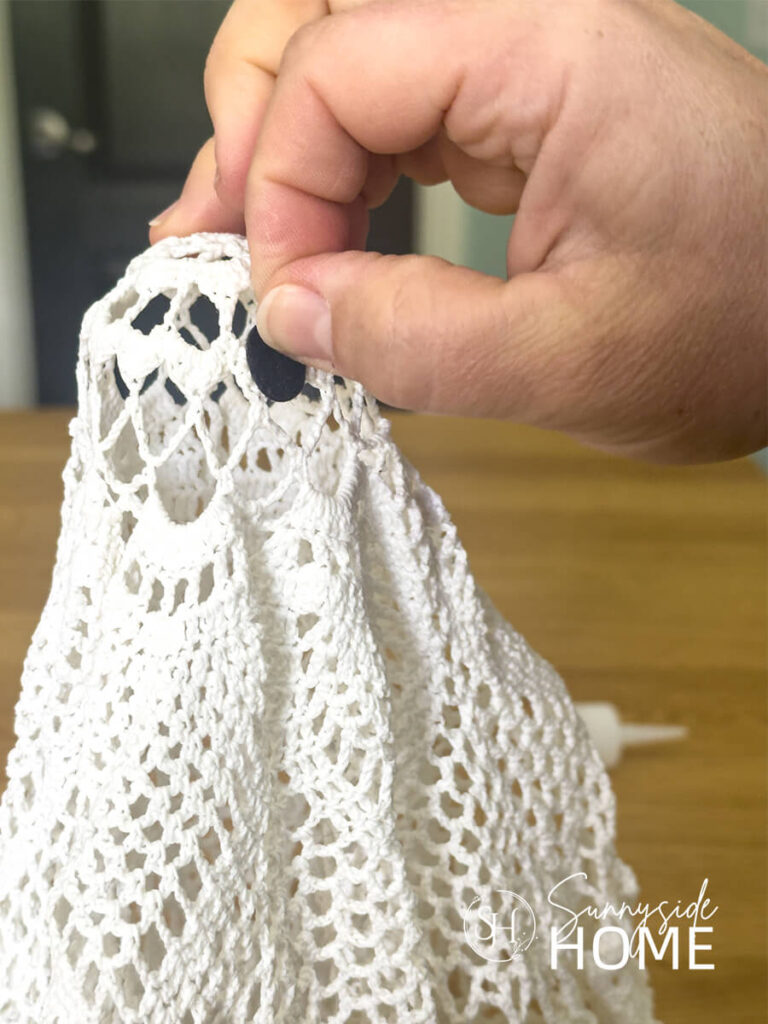 A woman places an oval black piece of felt on the dried vintage doily halloween ghost as an eye.
