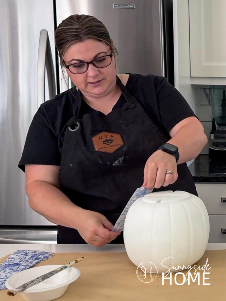 Woman places a strip of blue and white floral napkin to the pumpkin.