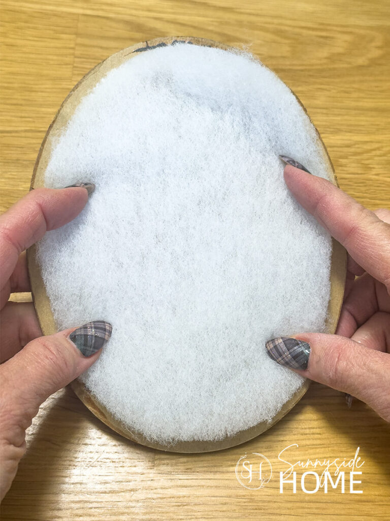 A woman places an oval piece of batting over the oval frame backing.