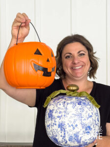 A woman holds an orange pumpkin trick or treat bucket and a DIY blue and white chinoiserie pumpkin embellished with a green velvet ribbon.