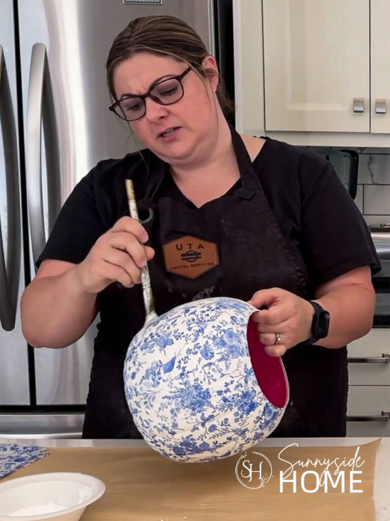 Woman applies Mod Podge decoupage medium to the blue and white pumpkin.