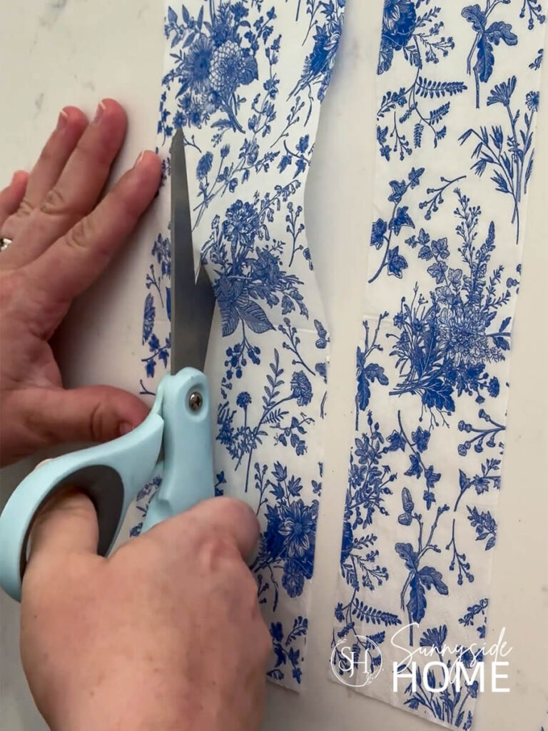 Woman cuts a blue and white floral napkin into 2" wide strips.