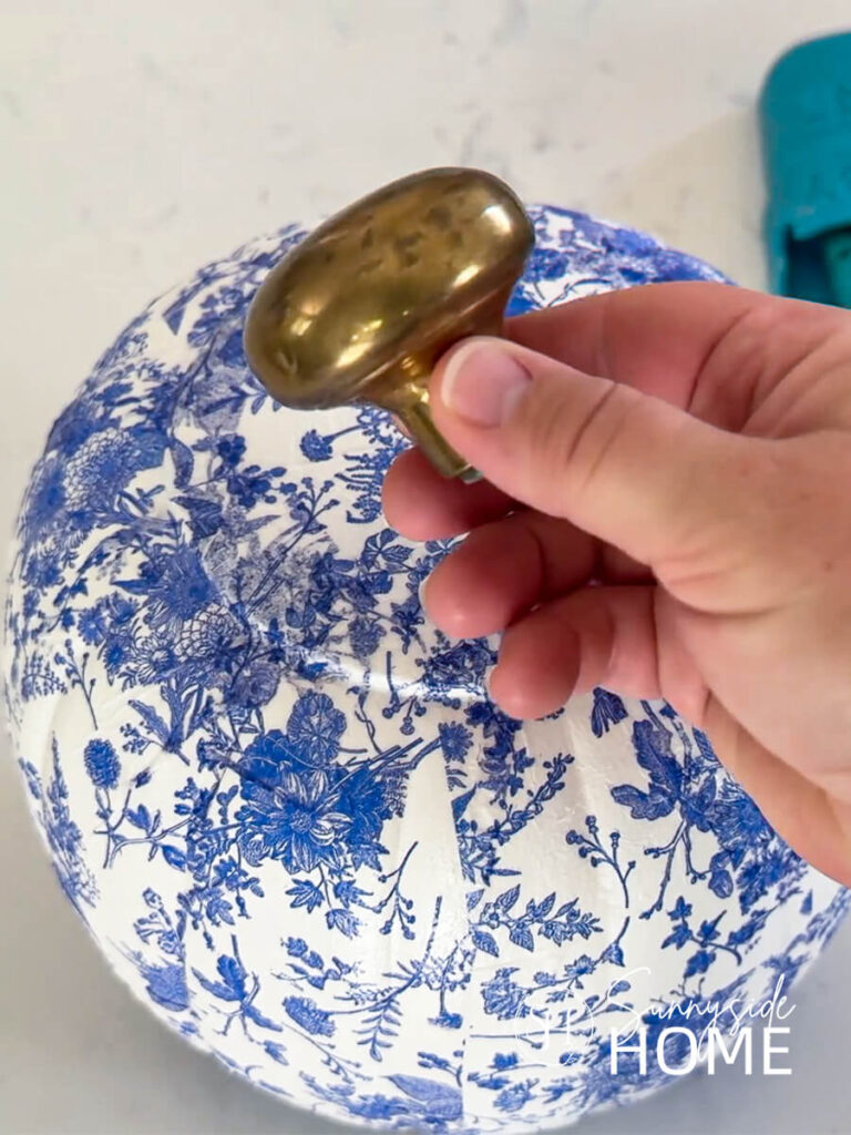 Woman holds a vintage brass door know that she will use as a stem on a blue and white chinoiserie pumpkin.