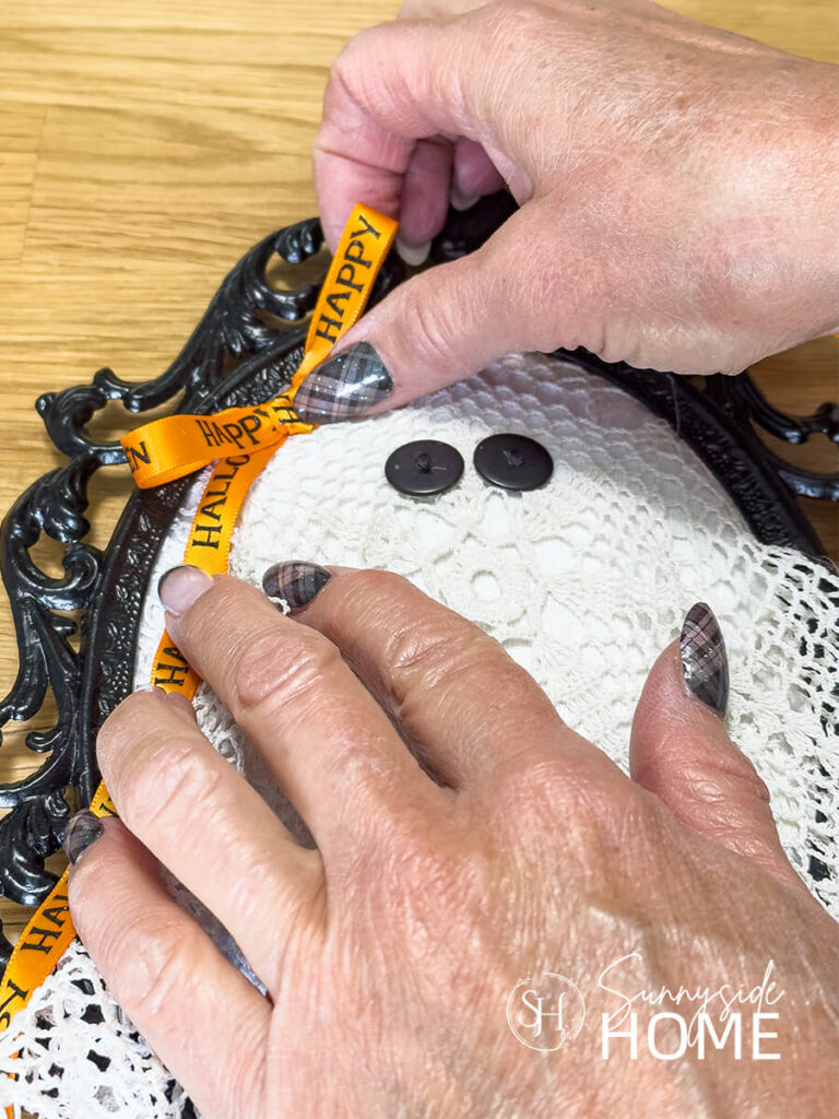 A orange happy Halloween ribbon is placed on the vintage lace doily ghost.