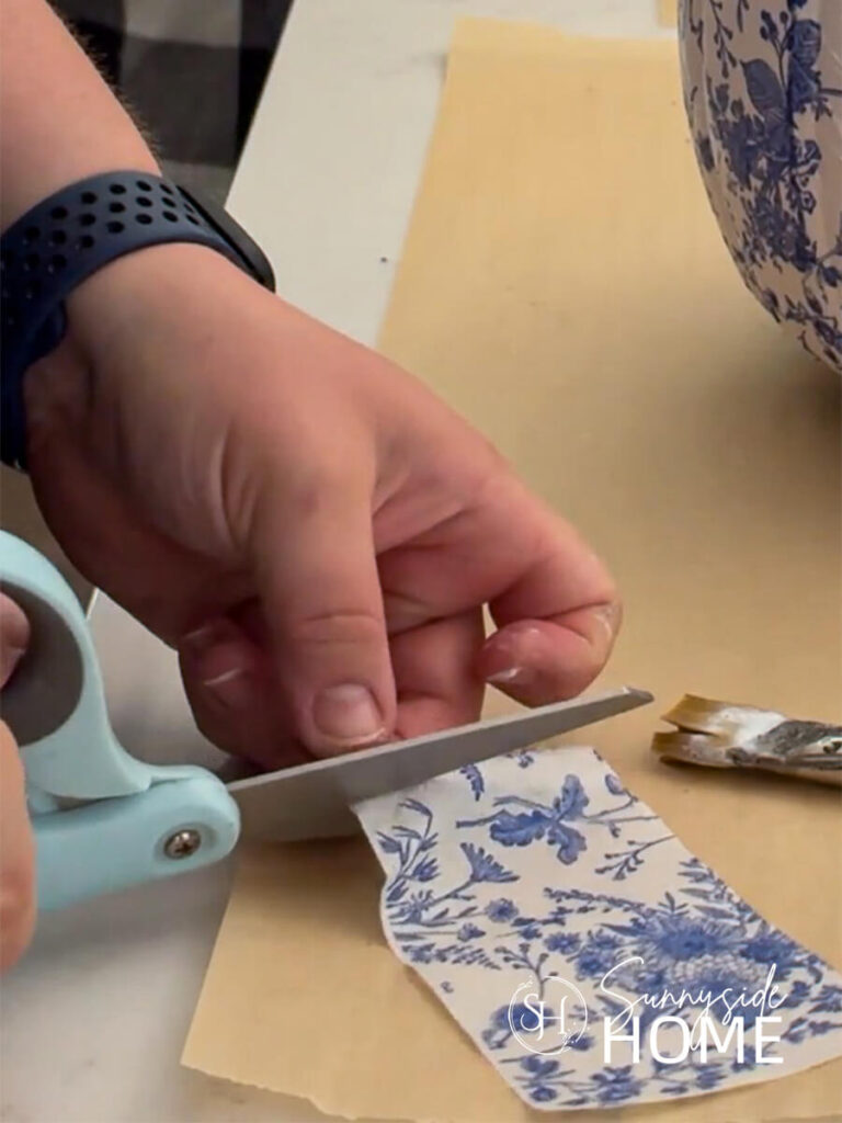 Woman uses scissors to trim a blue and white floral napkin.