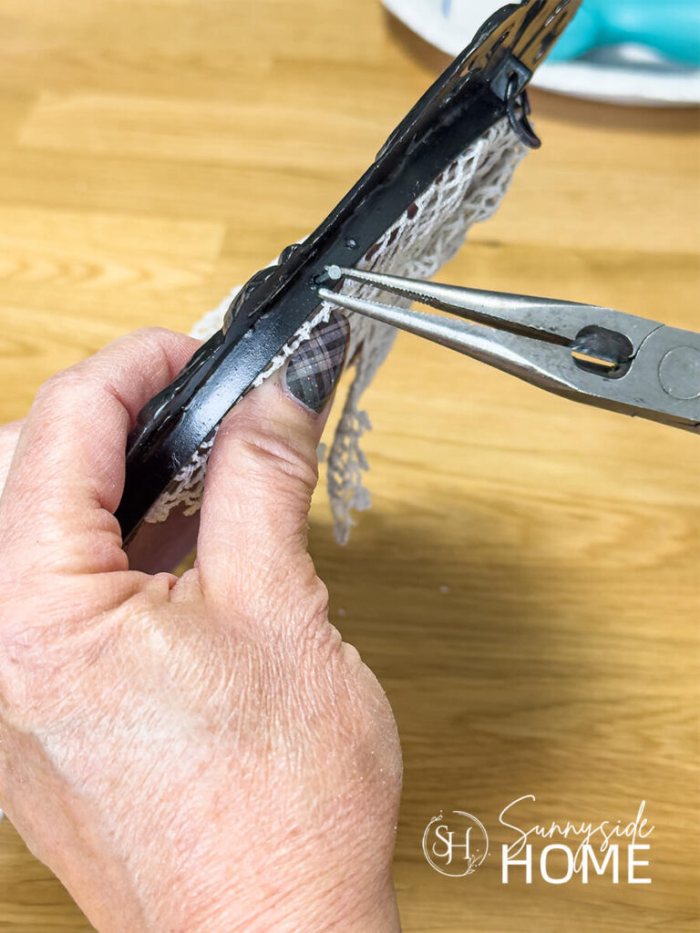 A woman places a small nail in the side of a frame to secure the frame back.