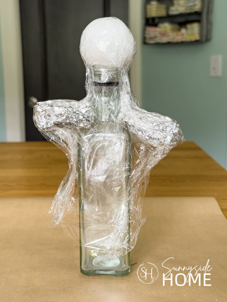 A form is made for making a doily ghost using a styrofoam ball, glass bottle, aluminum foil and plastic wrap.