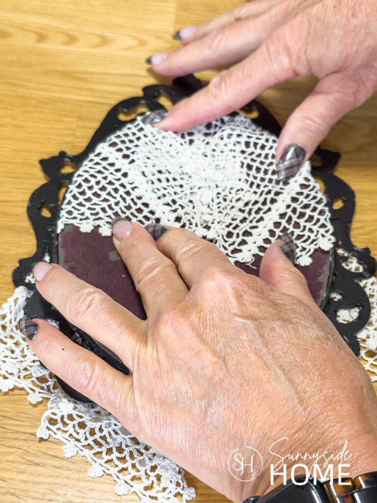 A woman presses the frame back into the frame after the doily has been wrapped around the frame.