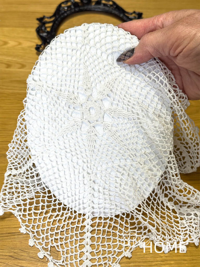 A woman places a vintage doily over an oval picture frame back.