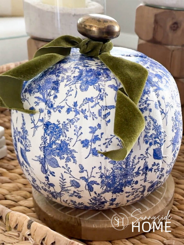 Styled blue and white chinoiserie decoupage pumpkins with pretty floral napkins, embellished with green velvet ribbon, styled in a basket with wood candleholders.