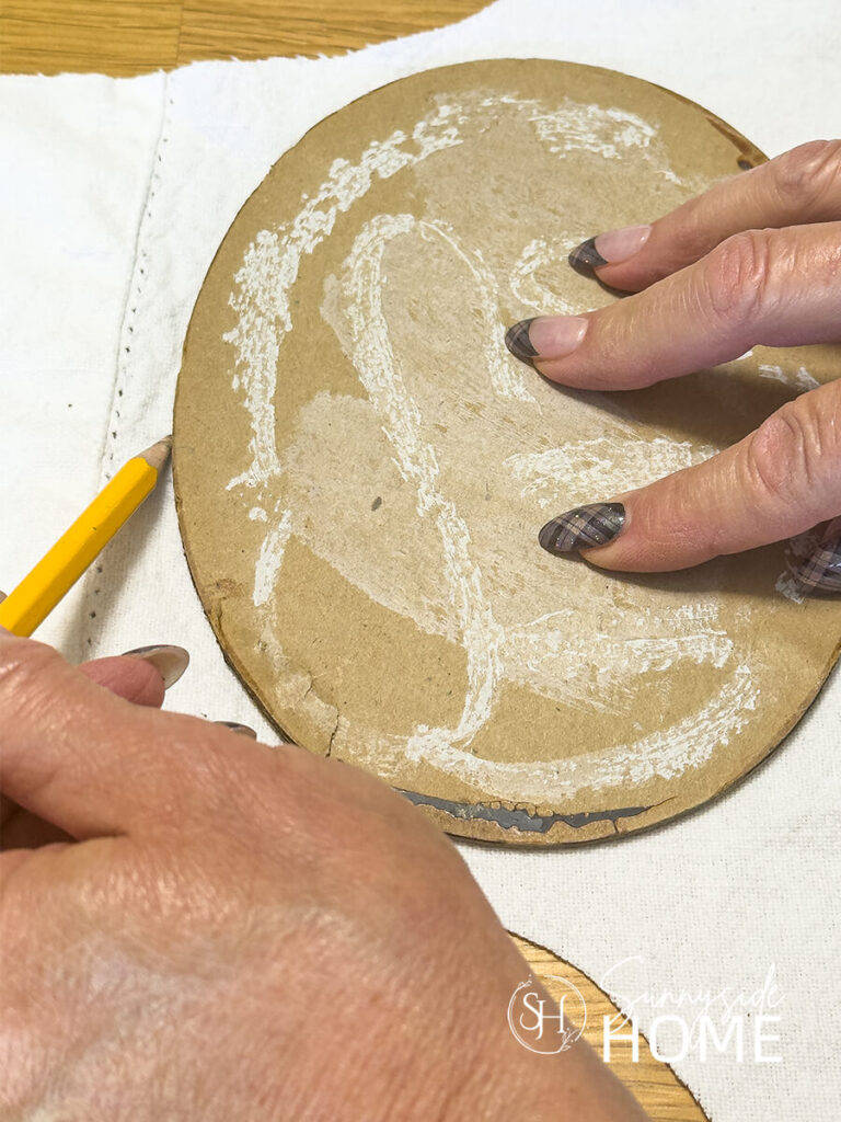 A woman holding a pencil. traces the shape of a frame back onto white fabric.