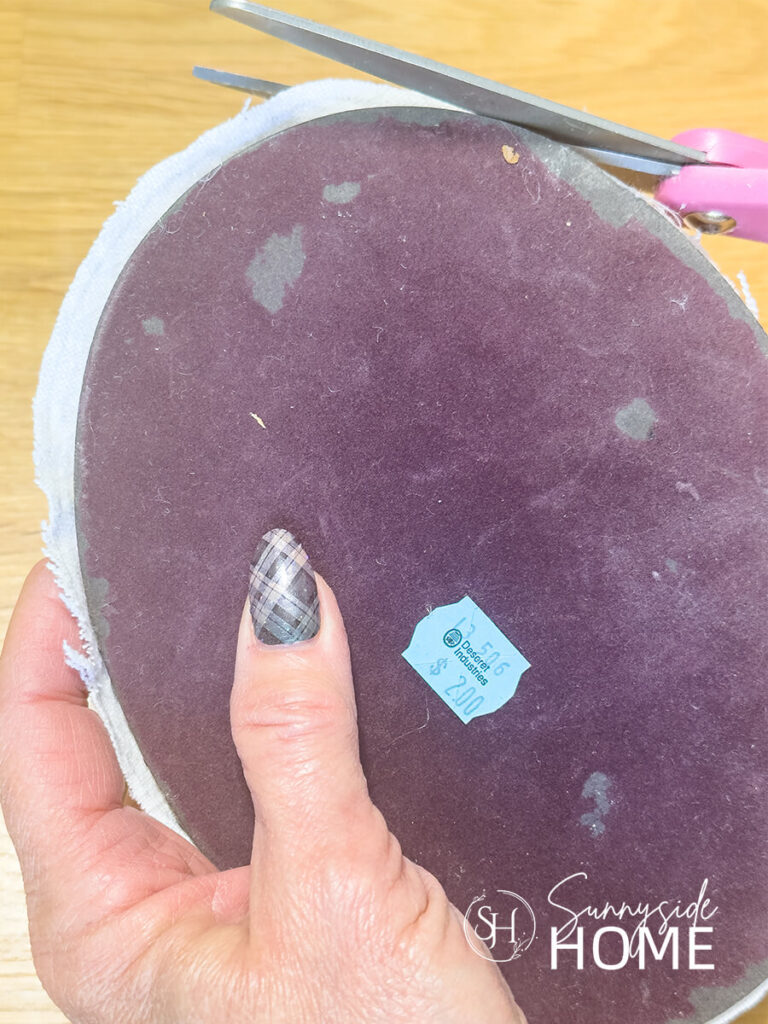 A woman trims excess fabric around the oval backing to a thrift store frame.