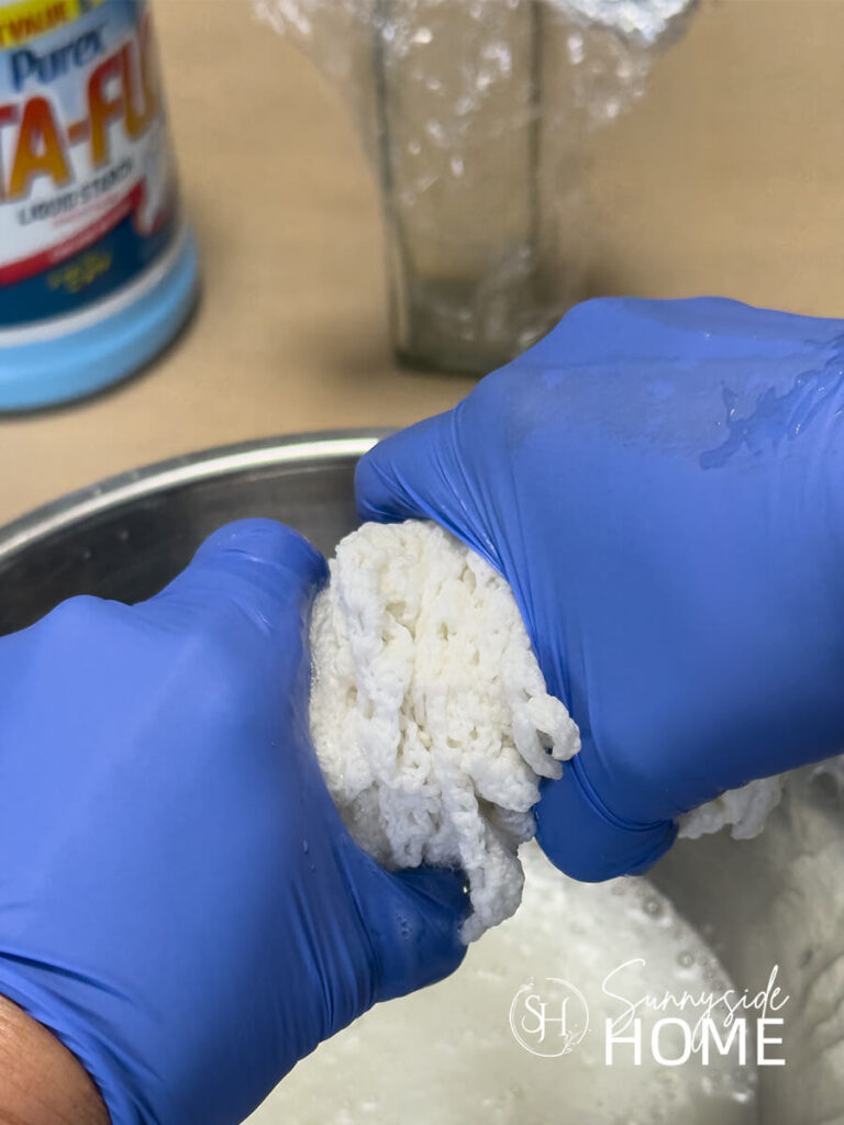 A woman wearing latex gloves wrings out excess fabric starch from a vintage doily.