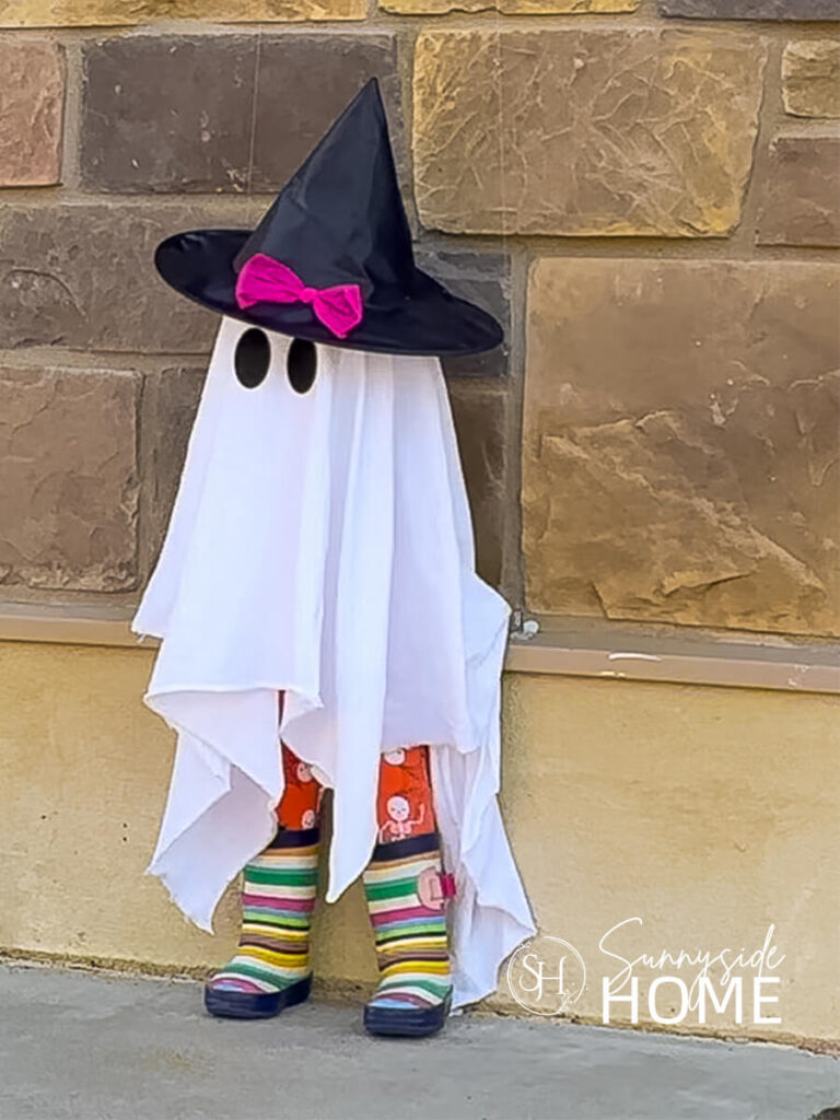 A cute child size ghost is made from thrifted rubber boots, Halloween leggings, witch hat and an old sheet. A pool noodle and styrofoam head are the base for this cute outdoor halloween decoration.