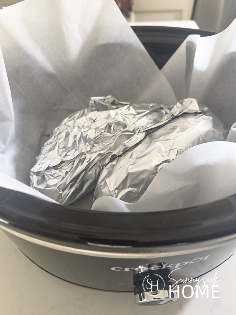 Foil wrapped sweet potatoes in a parchment lined slow cooker.