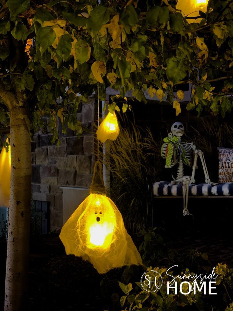 Glowing ghosts made with thrifted hair nets hanging from a tree with a skeleton in the background.