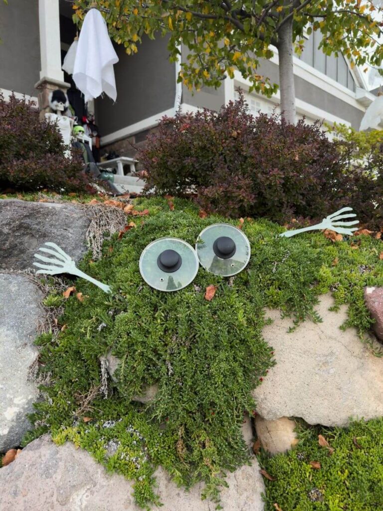 Silly Monster eyes in a garden made from pit lids and dollar store tongs, cute outdoor Halloween decor.