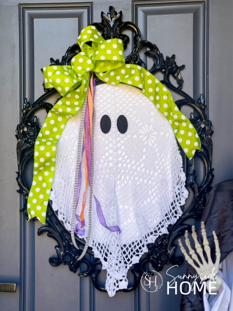 An old frame is transformed into a cute vintage ghost with thrift store crocheted lace and embellished with Halloweens as a creative Halloween wreath.