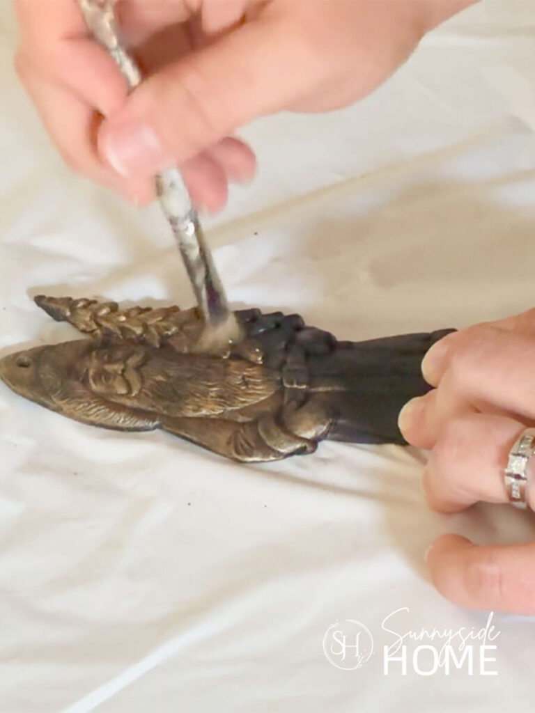 Woman applies gold rub n buff with an old paint brush to a black painted clay Santa ornament.