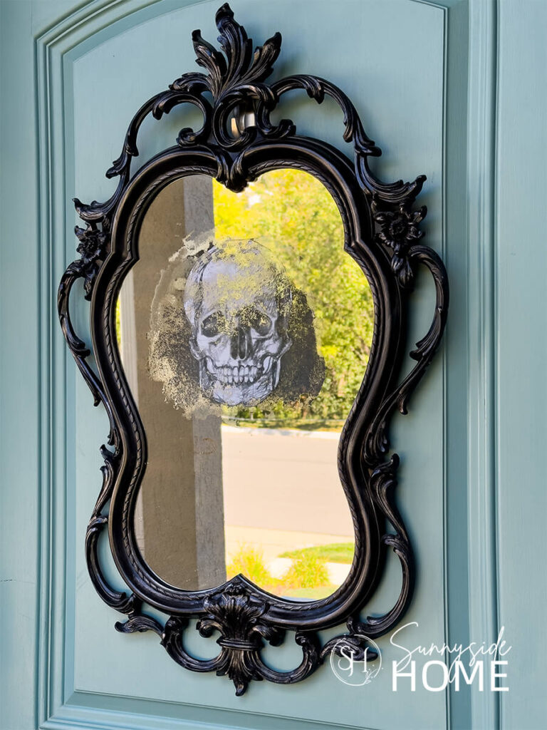 A thrift store mirror is transformed for Halloween with black spray paint and a skeleton sketch and hung on the front door as a wreath.